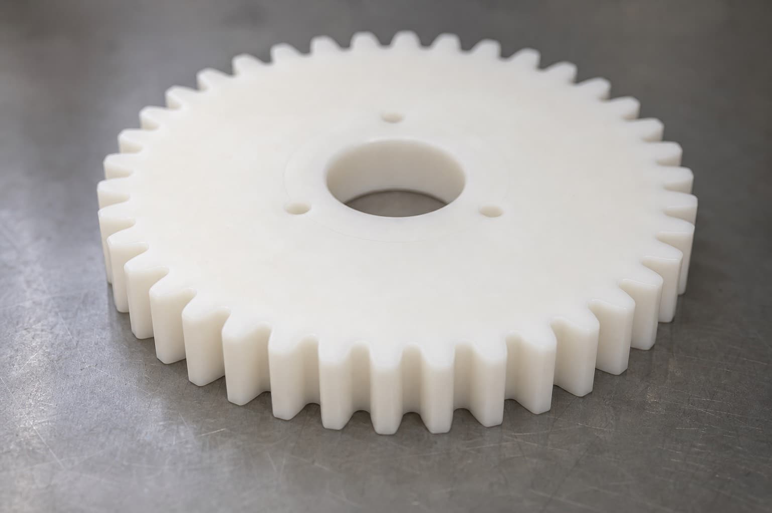 Close-up of a white acetal spur gear showing full-depth teeth, root fillets, and a machined center bore.