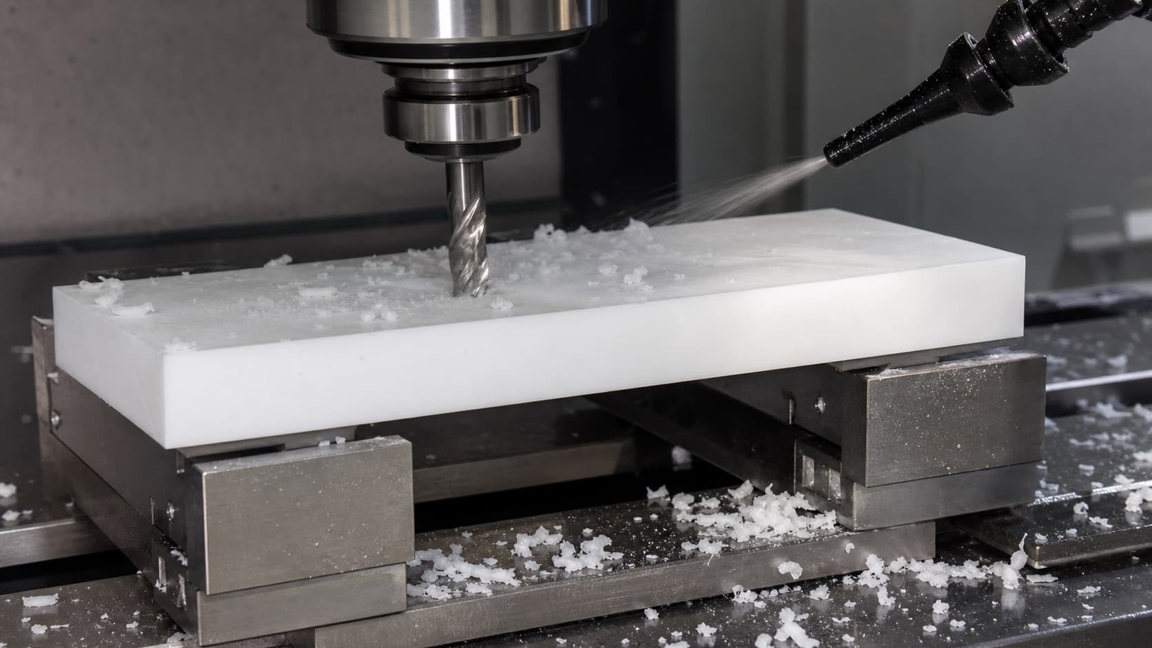 CNC mill face milling a white acetal block while compressed air clears short plastic chips