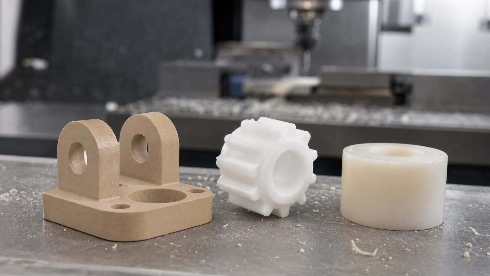 Tan PEEK bracket, white Delrin gear, and natural nylon spacer on a CNC shop bench