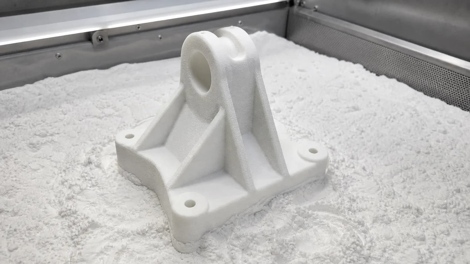 White powder-bed printed bracket sitting in nylon powder